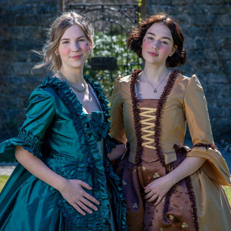 Two young women wearing period costume. The dresses are made of satin.